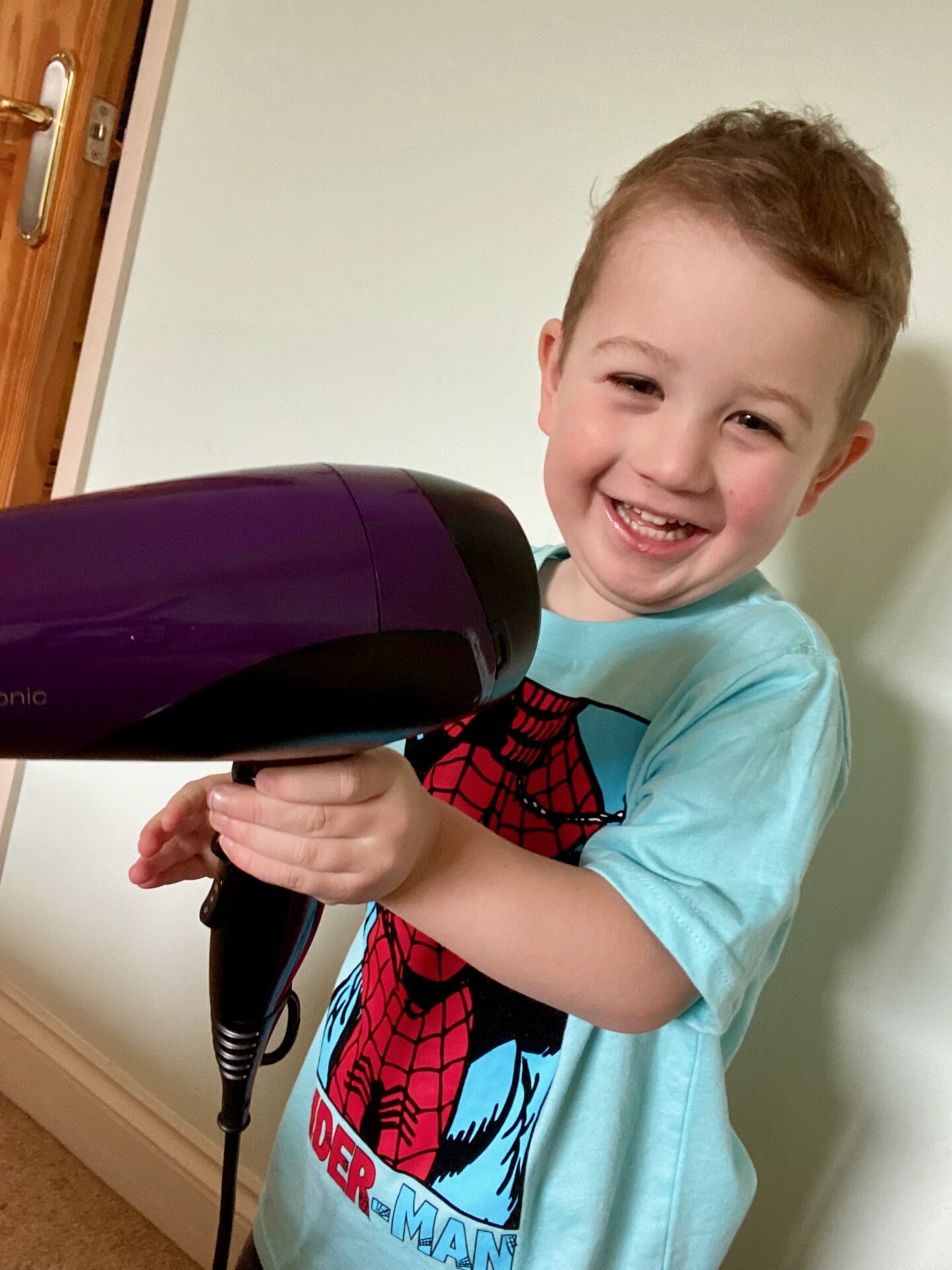 3 year old smiling boy holding a hair dryer